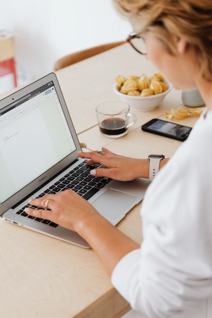 Alt text: Person typing on a laptop at a desk with coffee and snacks nearby.